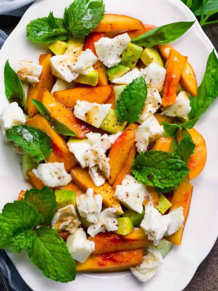 Peach salad with mozzarella on a white platter.
