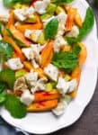 peach mozzarella salad featuring sliced peaches, mozzarella, fresh mint and basil leaves on a white dish.