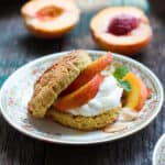 A shortcake split in half and filled with peaches and whipped cream on a plate.