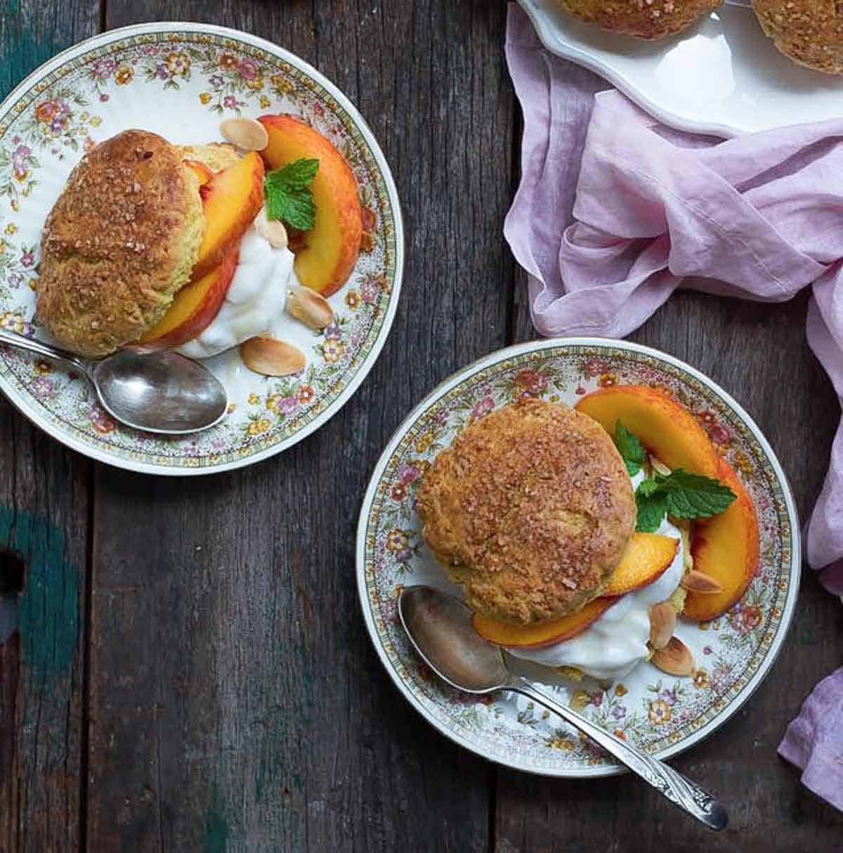 2 plates with shortcakes, peaches, and cream with a napkin on the side.