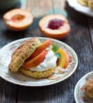 A shortcake split in half and filled with peaches and whipped cream on a plate.