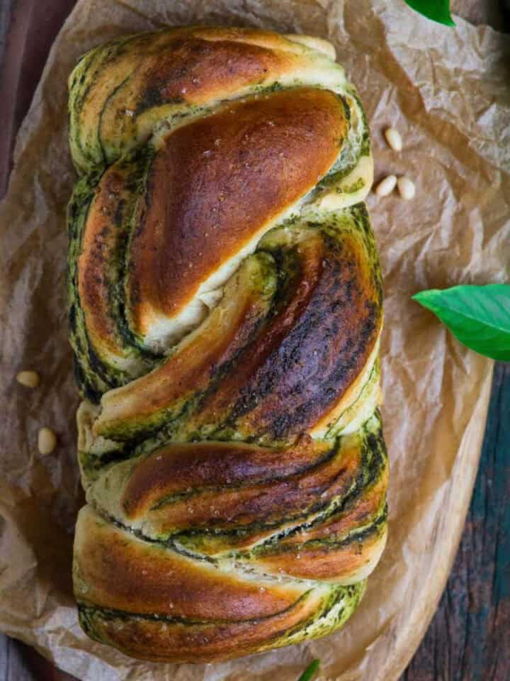 Braided pesto bread on parchment paper with ingredients around.