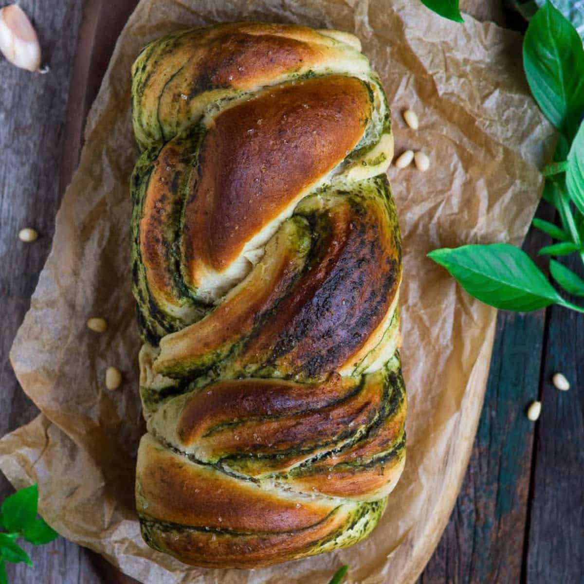 Braided pesto bread on parchment paper with ingredients around.