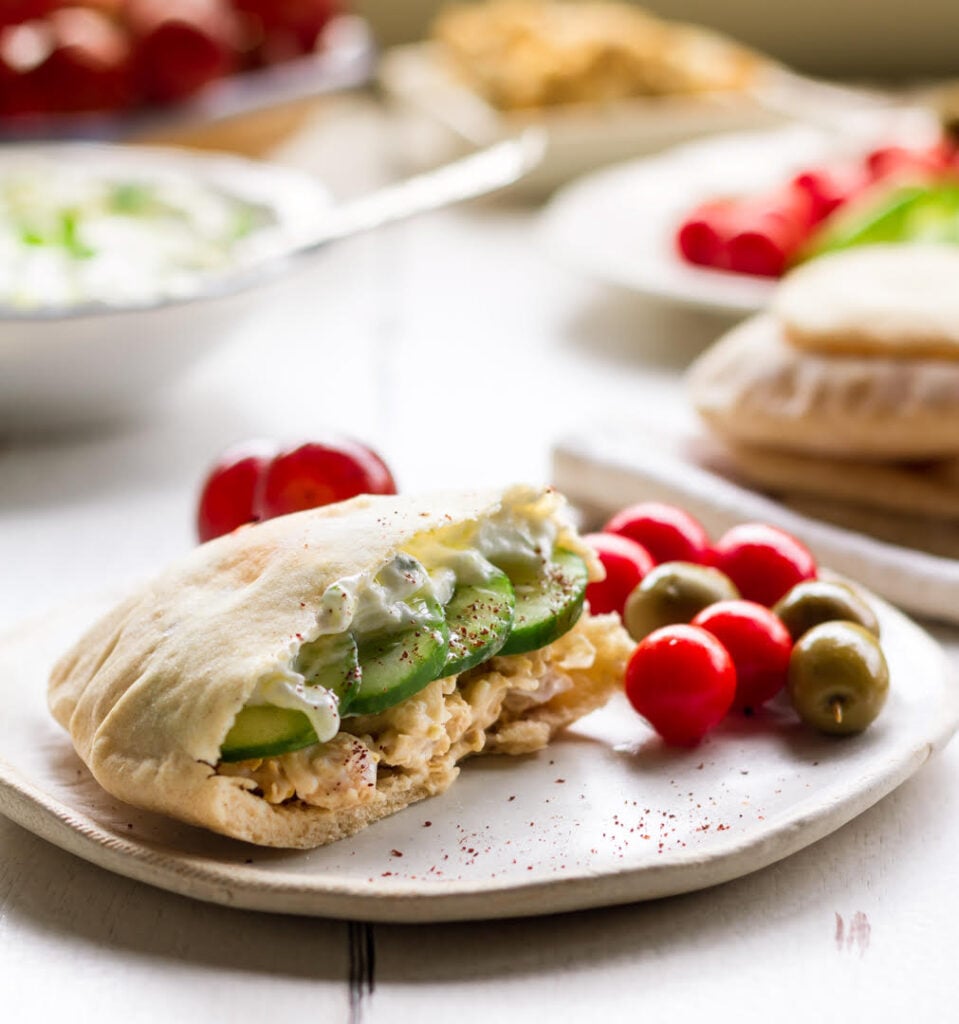 Half a pita sandwich on a plate with cherry tomatoes and olives.
