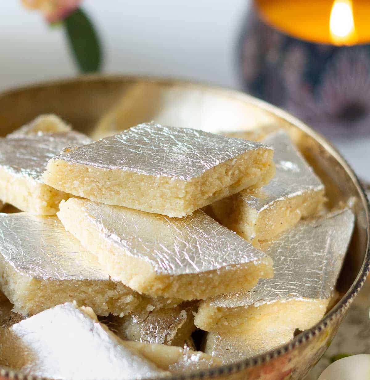 Kaju burfi pieces in a bowl with a candle in the background.