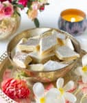 Kaju burfi in a bowl with flowers and candle around.
