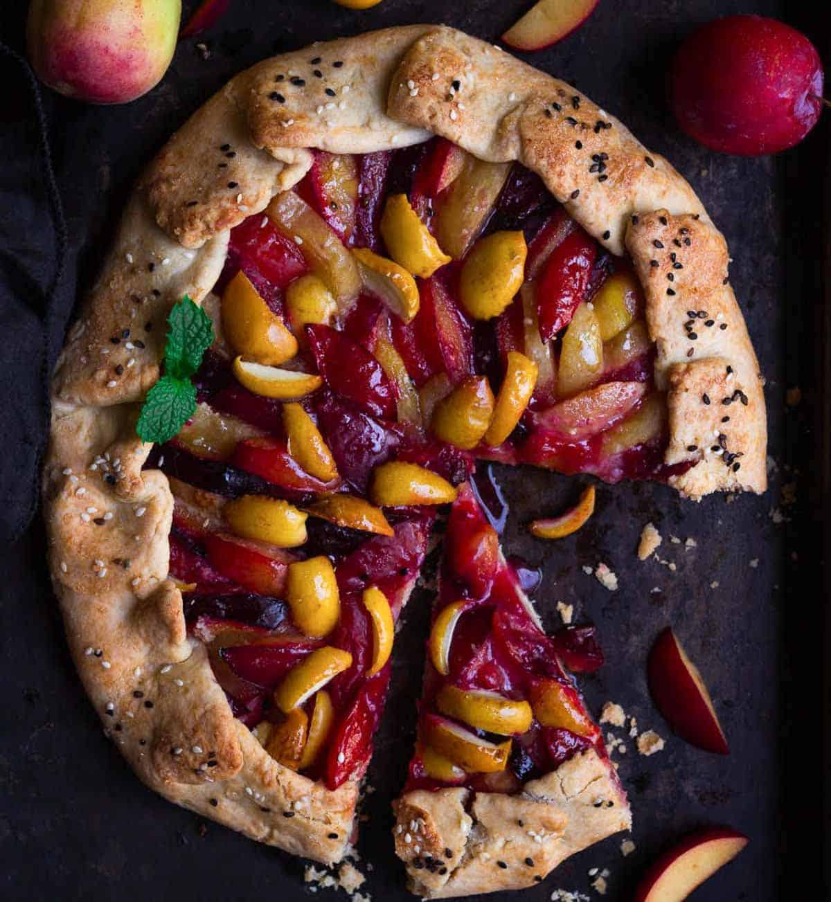 A fruit galette on a black tray with one slice cut.