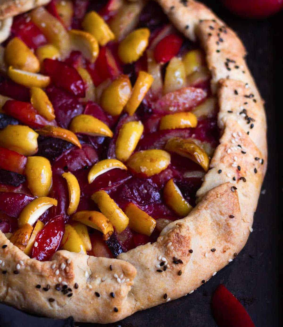 A galette with  sesame seeds on its crust and filled with plums and apricots.