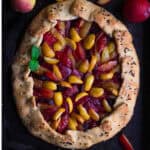 A galette with plums and apricots on a black tray.