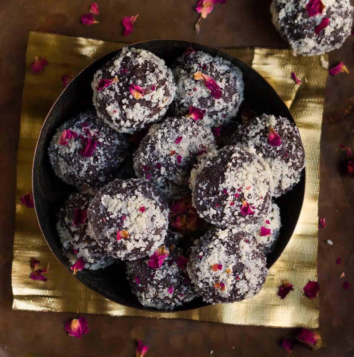 A bowl of chocolate pedas garnished with rose petals and flowers around.