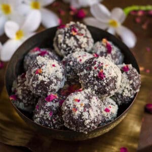 Chocolate pedas rolled in almond meal garnished with dried rose petals in a bowl.