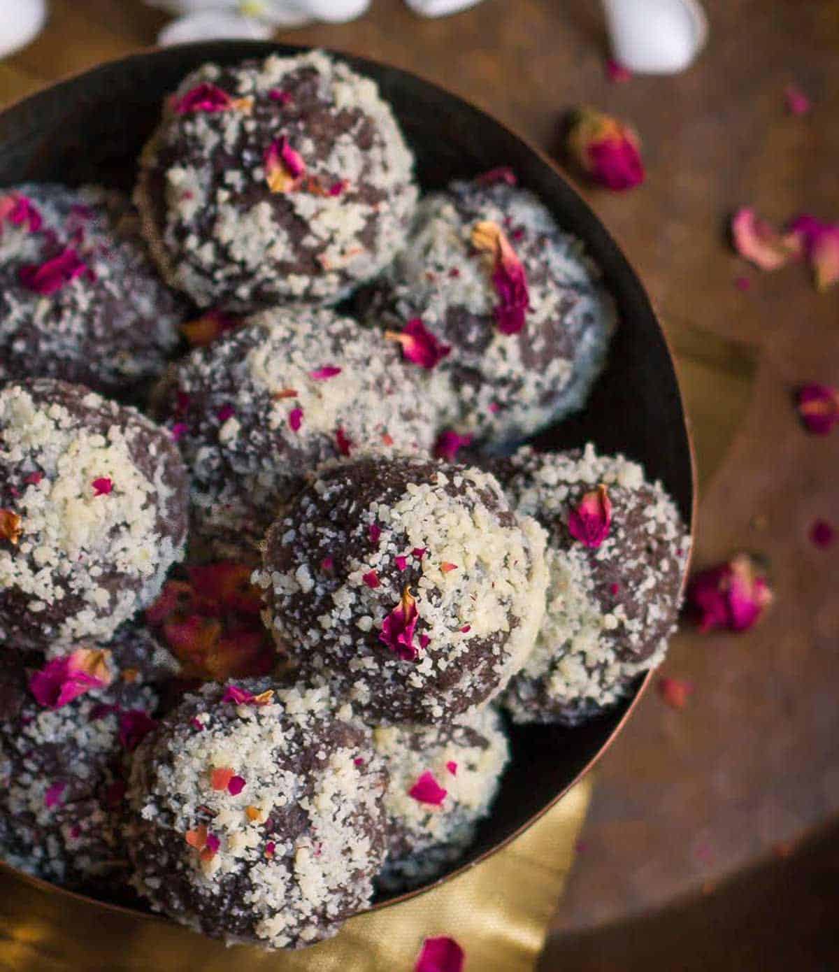 A bowl filled with chocolate pedas garnished with dried rose petals.