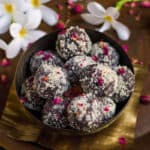 Chocolate pedas rolled in almond meal garnished with dried rose petals in a bowl.