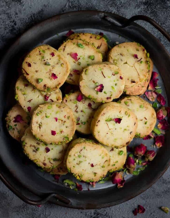 Rose pistachio cookies in a serving tray garnished with dried rose buds.