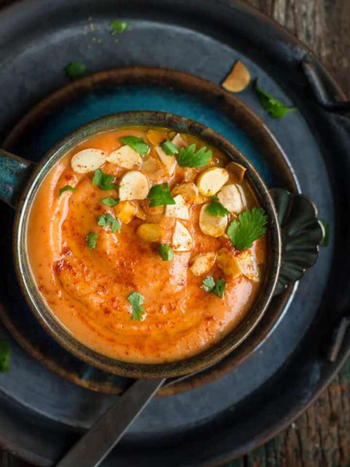 A bowl of roasted carrot soup garnished with almonds on a tray.