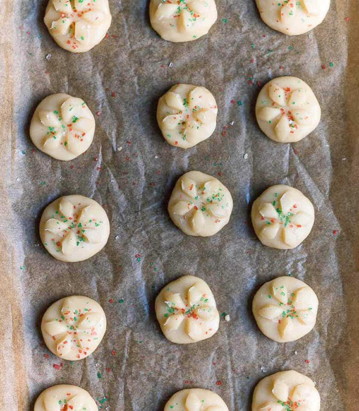 Cookie dough balls with red and green sprinkle on top on parchment paper.