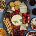 A silver cheese platter with cheese, soup sticks, crackers,fruits, olives, nuts and jam.