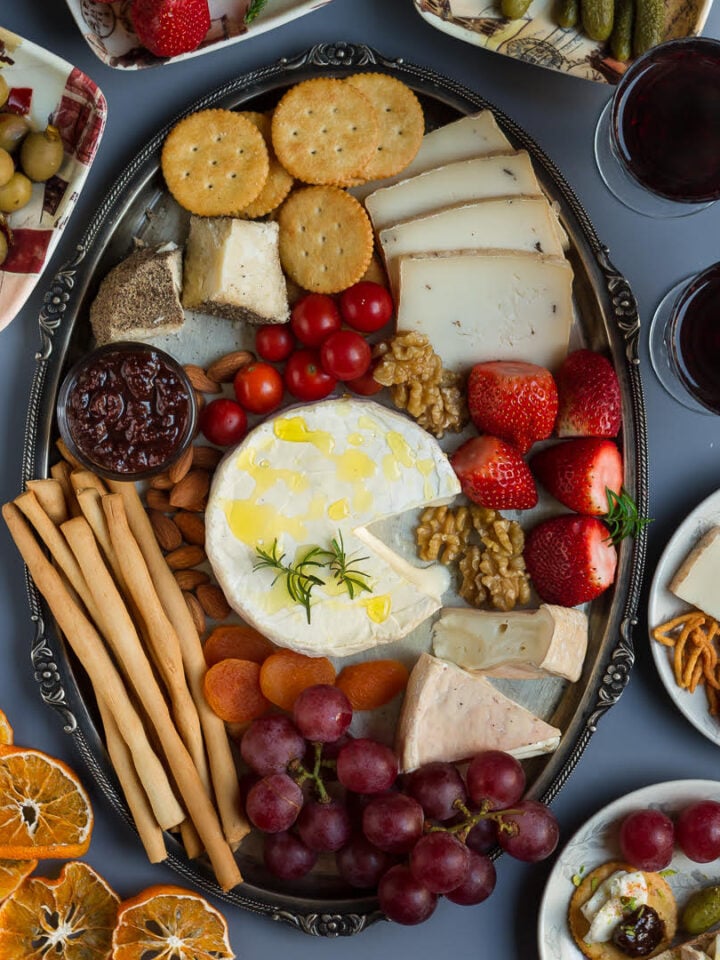 A silver cheese platter with cheese, soup sticks, crackers,fruits, olives, nuts and jam.