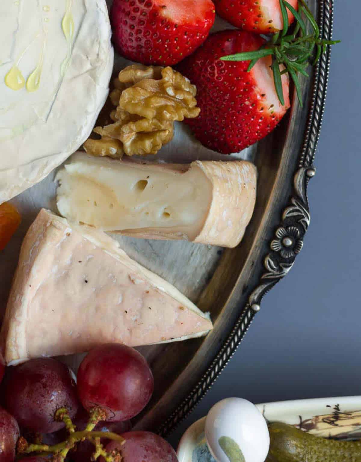 Reblochon style rind cheese with fruits and nuts on a silver platter.
