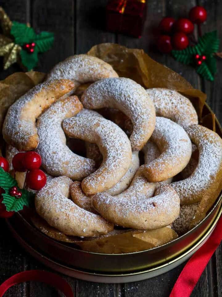 Lemon crescent cookies in a tin box with christmas decorations around.