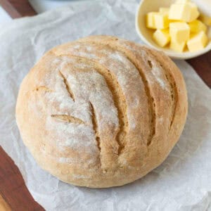 A loaf of sourdough discard bread on parchment paper with a dish of butter on the side.