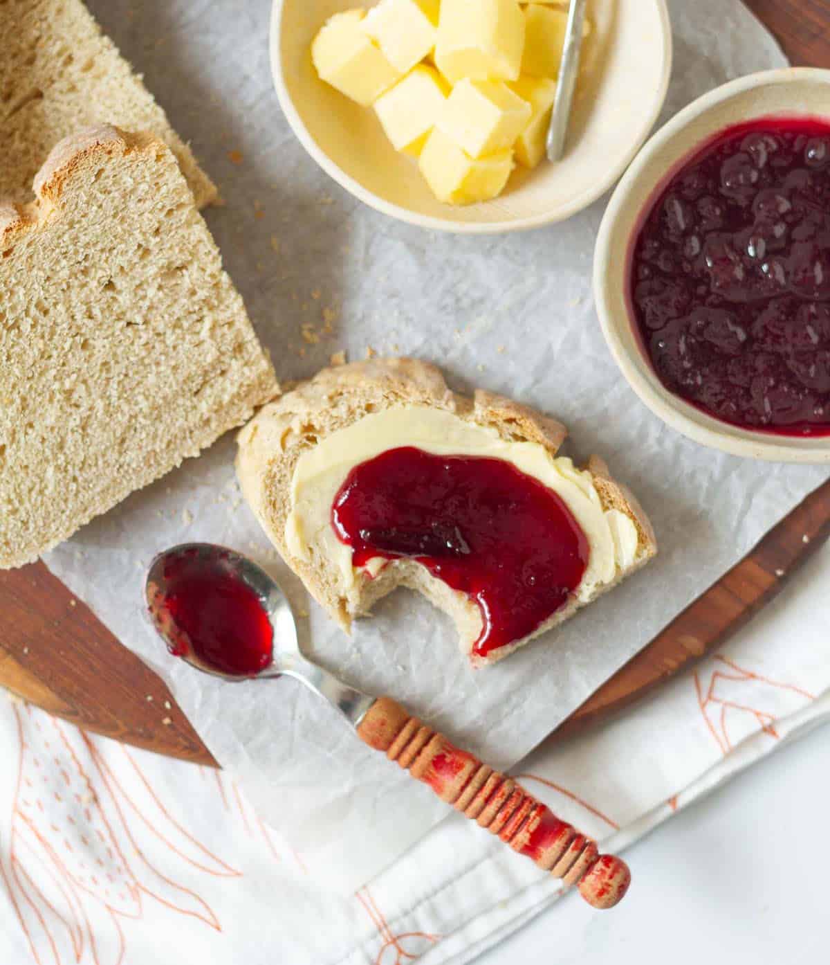 A slice of bread with a bite taken topped with butter and jam on parchment paper.