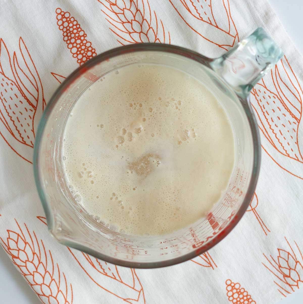 A measuring cup with frothy yeast and water mixture.