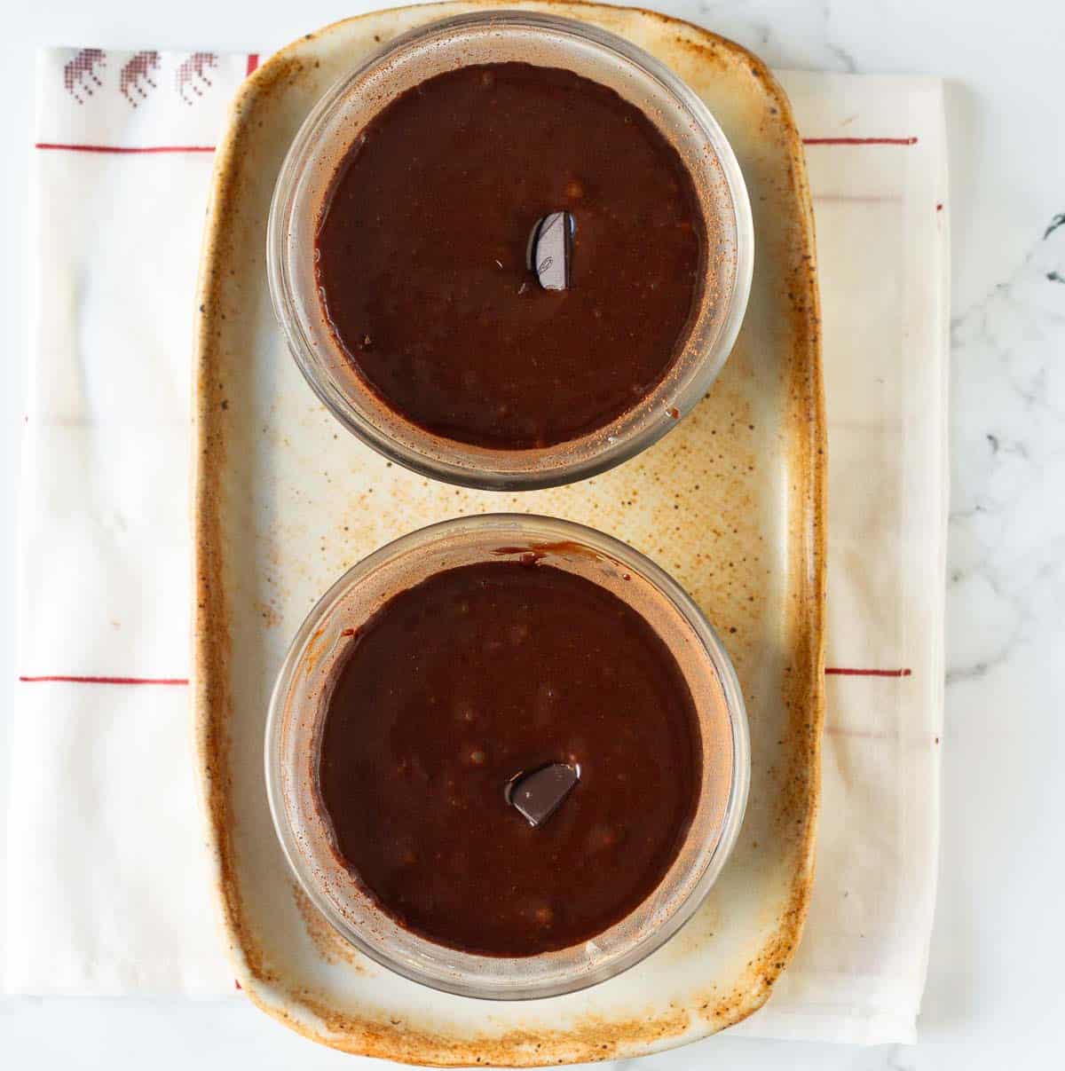 Chocolate batter in 2 ramekins with chocolates in the center.