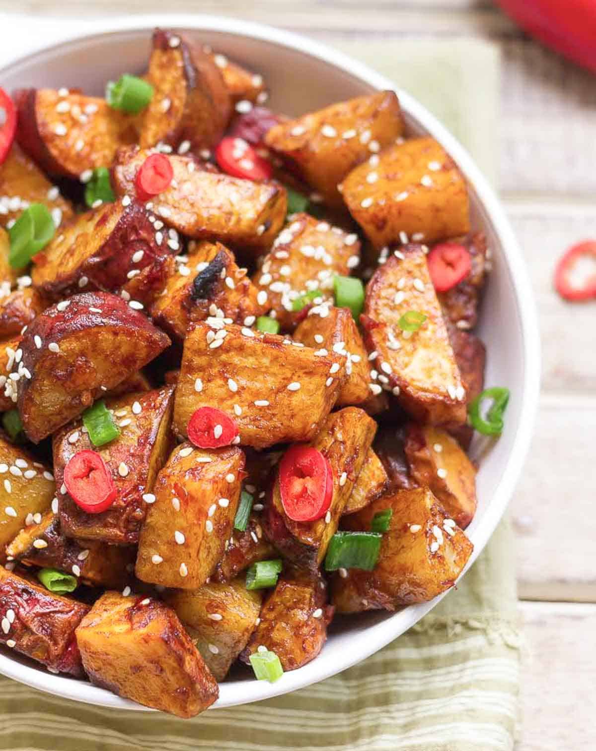 Glazed sweet potatoes in a bowl, garnished with sesame seeds and spring onions.