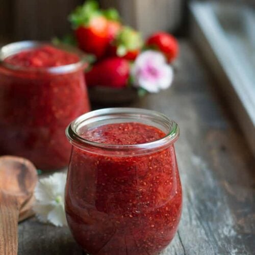 Strawberry chia seed jam in 2 glass jars with flowers in the background.