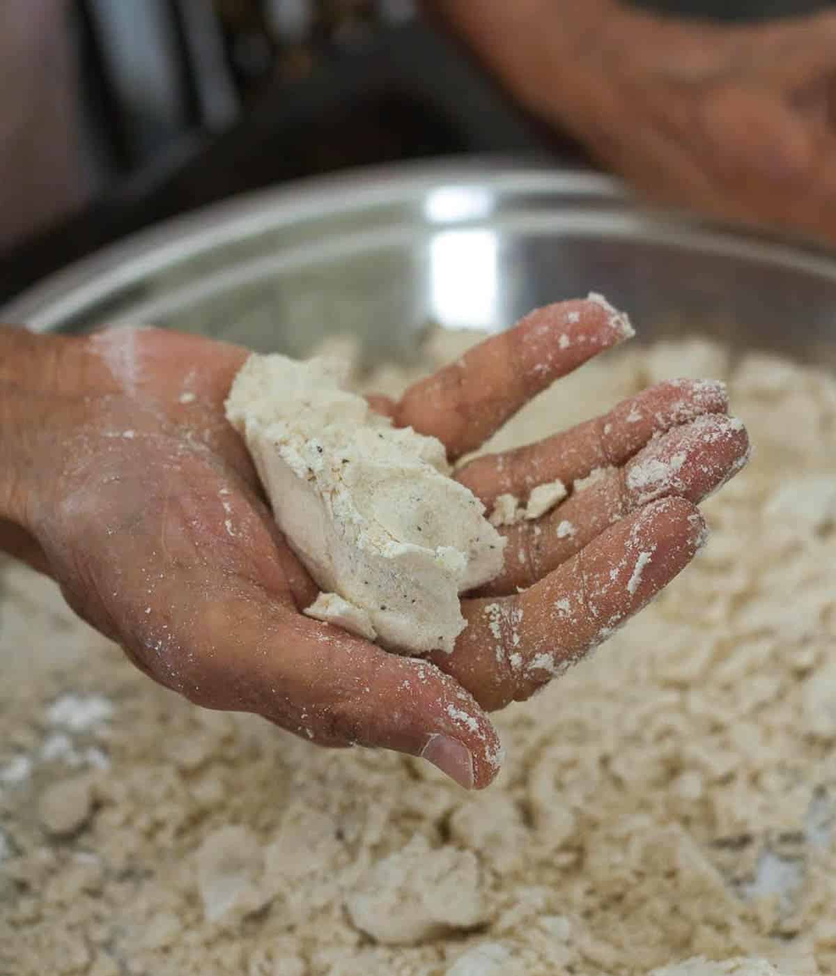 a hand holding dough on top of a plate with dough.