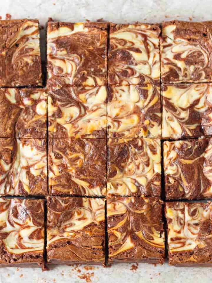 Cheesecake swirl brownies cut into 16 squares on parchment paper.