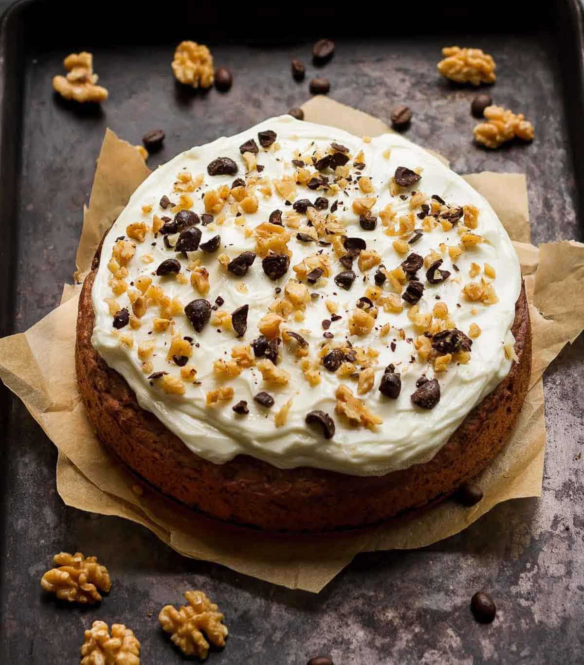 Cake with creamy frosting and walnuts on top on parchment paper.