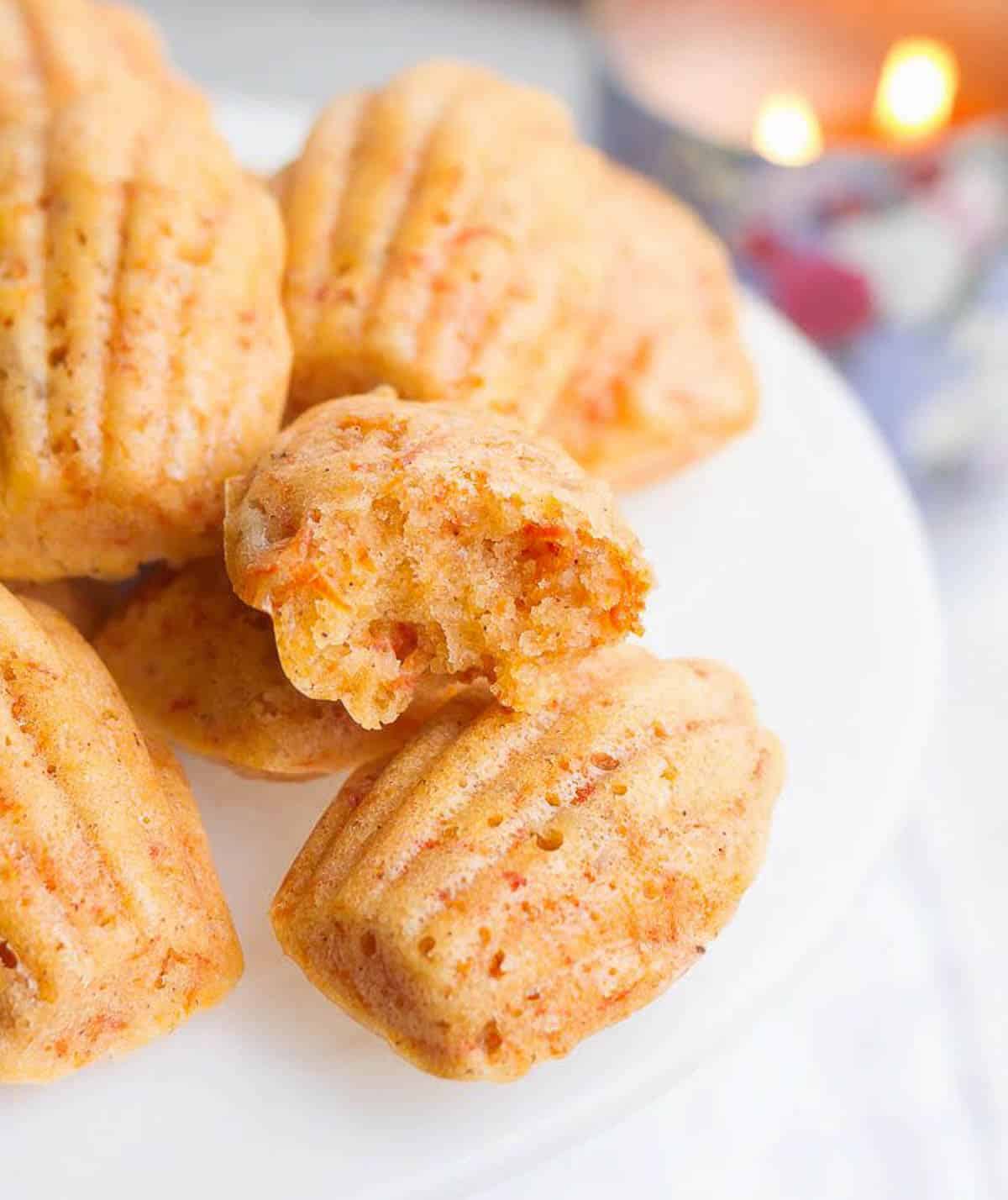 Madeleines on a cake stand with one madeleine cut into half to show the texture.