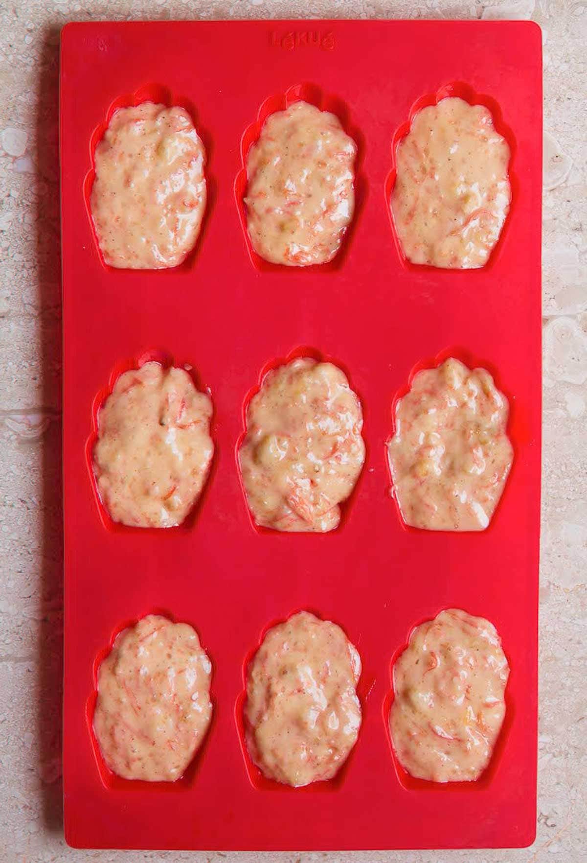 Madeleine batter spooned into a red silicone mold.