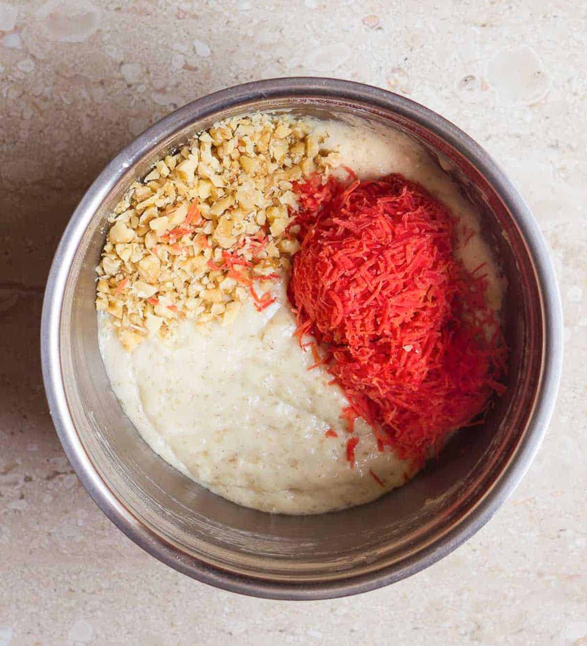 shredded carrots and walnuts on top of the batter in a mixing bowl.