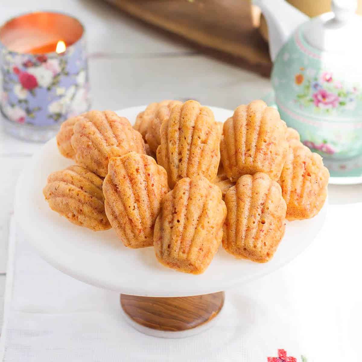 carrot cake madeleines on a cake stand with a candle and teapot in the background.