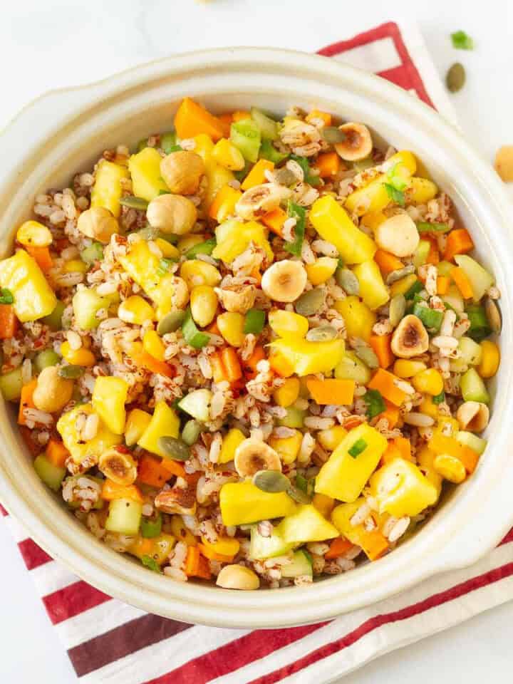 A bowl of rice and mango salad on a red and white napkin.