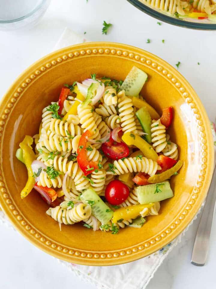 Pasta salad with veggies in a yellow bowl, with a fork on the side.