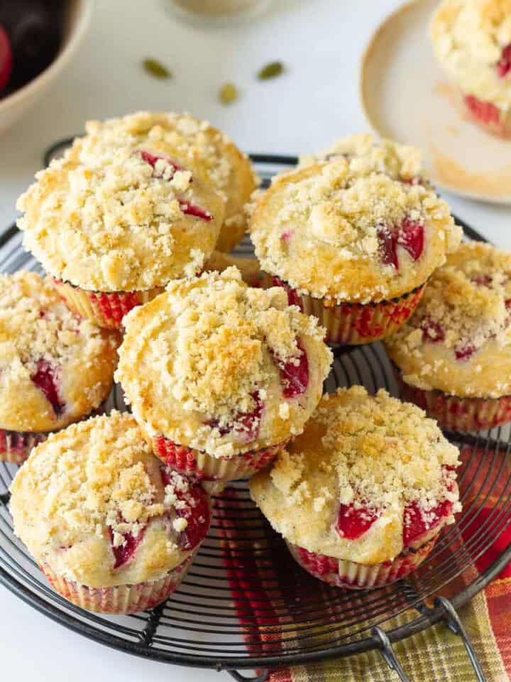 Plum muffins with streusel stacked on a round wire rack.
