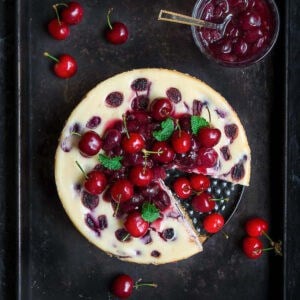 Cherry cheesecake topped with cherry compote on a tray with a slice taken out.