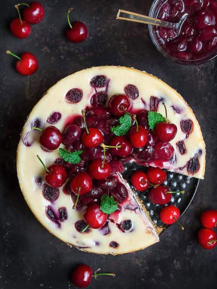 Cherry cheesecake topped with cherry compote on a tray with a slice taken out.