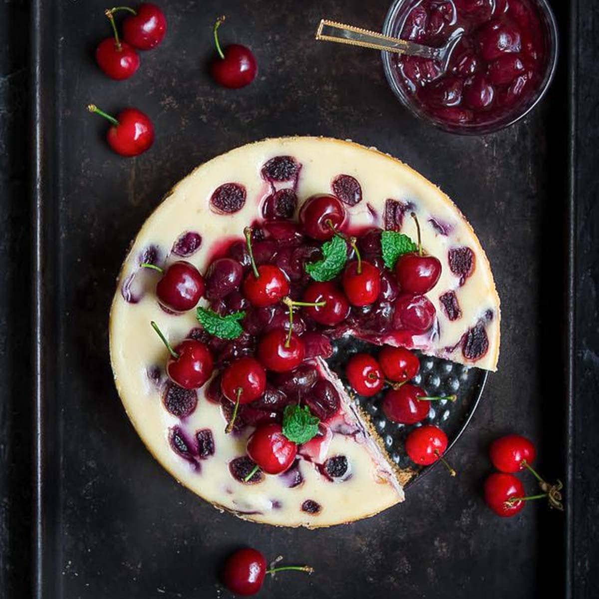 Cherry cheesecake topped with cherry compote on a tray with a slice taken out.