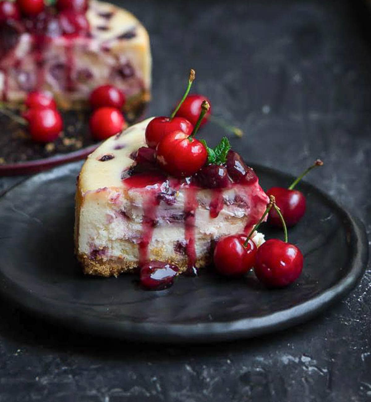 A slice of cherry cheesecake on a small plate with cherry compote on top.
