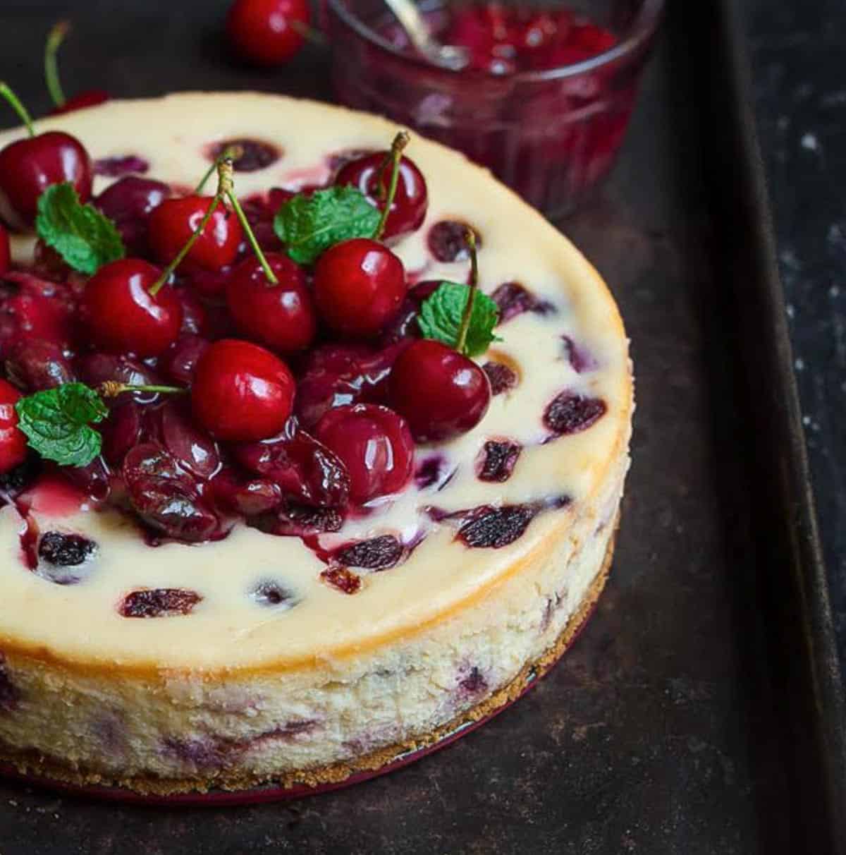 cheesecake with cherries and cherry sauce on a black tray.