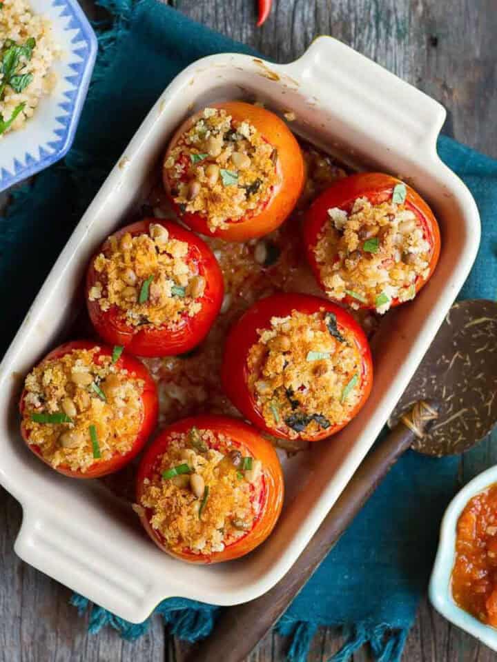Baked stuffed tomatoes in a rectangular baking dish with ingredients around.