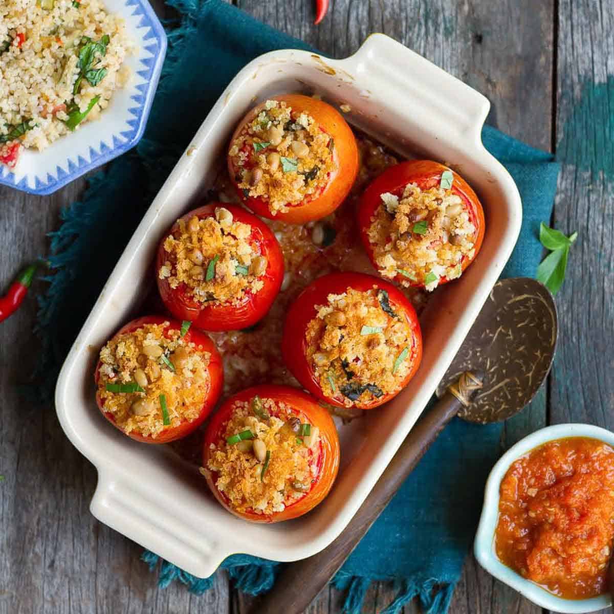 Baked stuffed tomatoes in a rectangular baking dish with ingredients around.