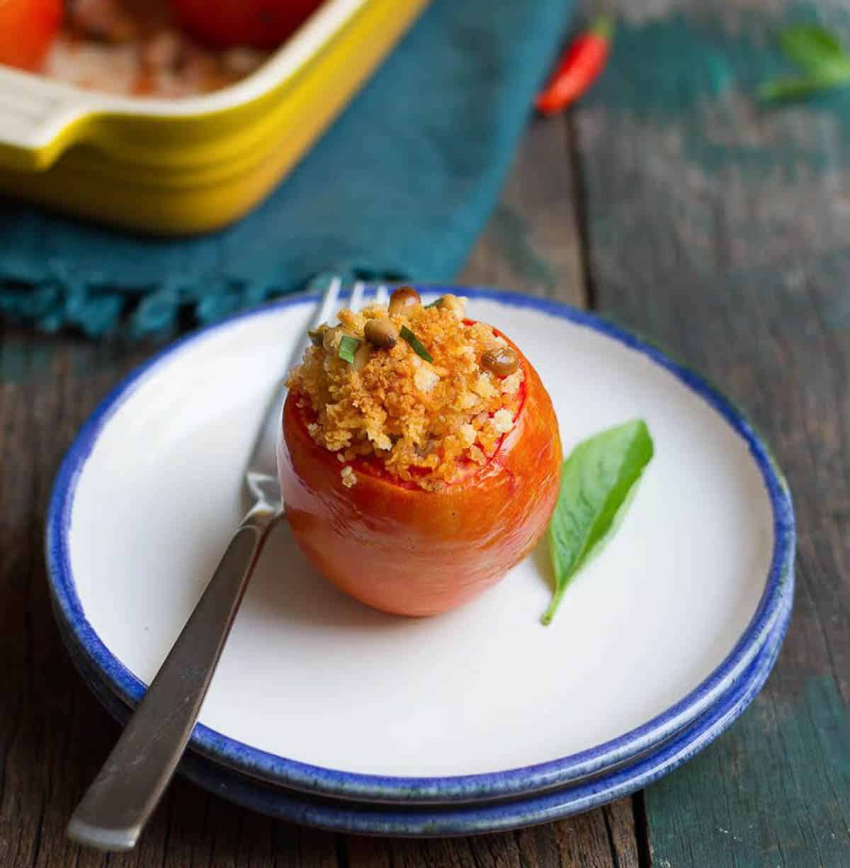 A stuffed baked tomato with a fork on a plate.