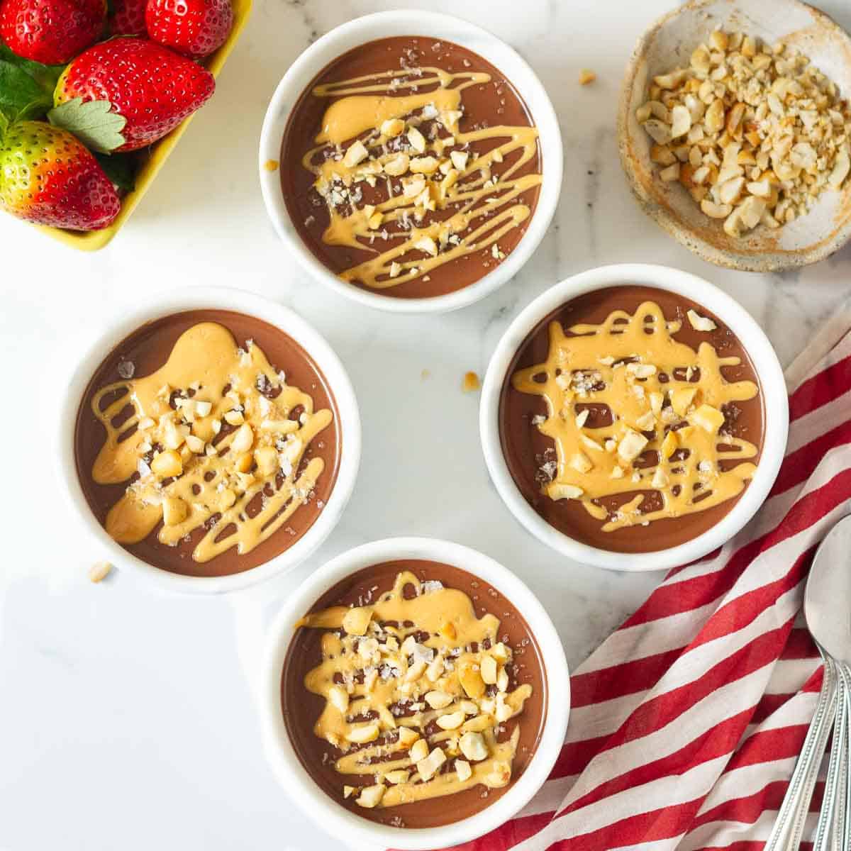 4 bowls of chocolate pudding garnished with peanut butter, chopped peanuts and sea salt.