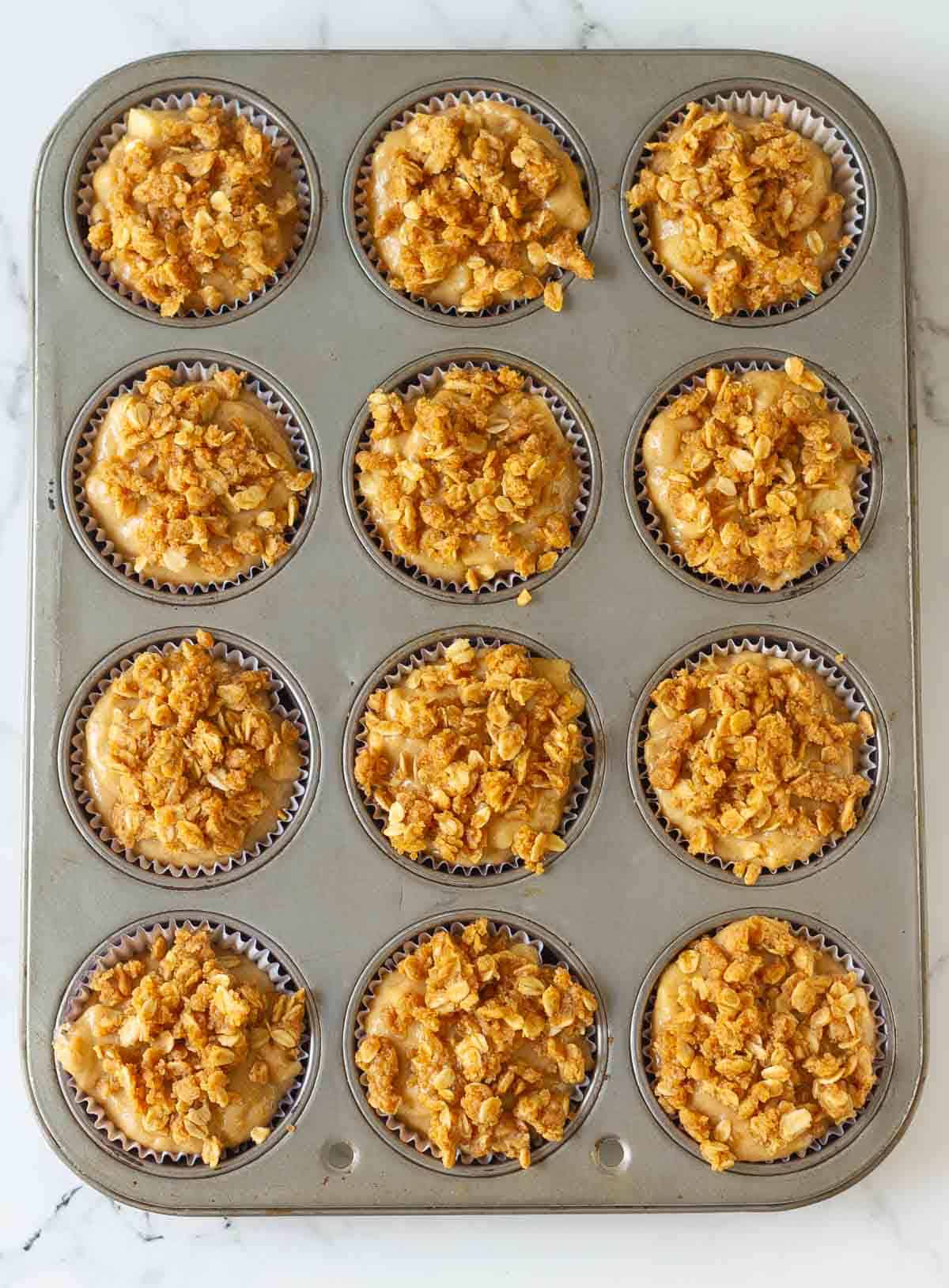 Oats streusel on top of muffin batter in a muffin tray.